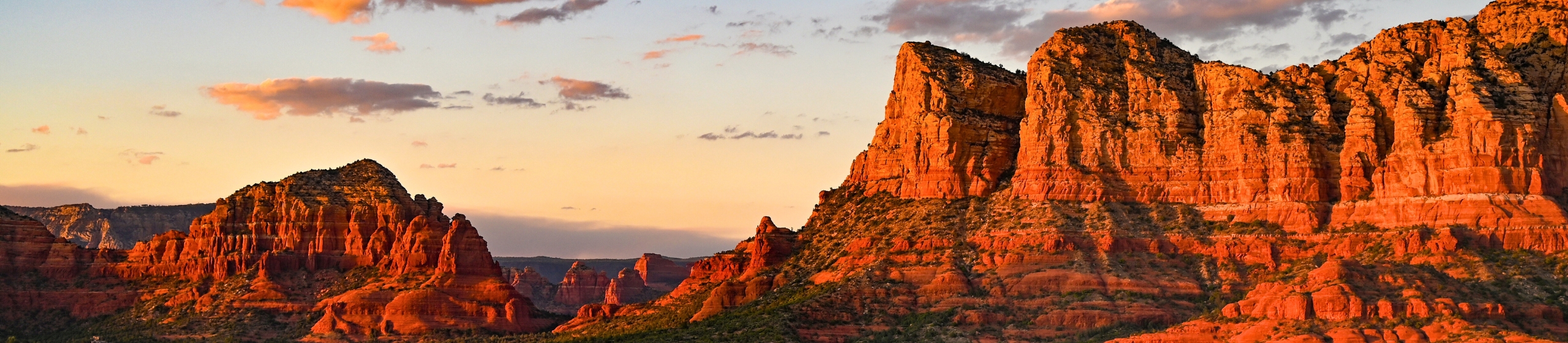 Red rock formations at sunrise in Sedona, Arizona, glowing with warm light.