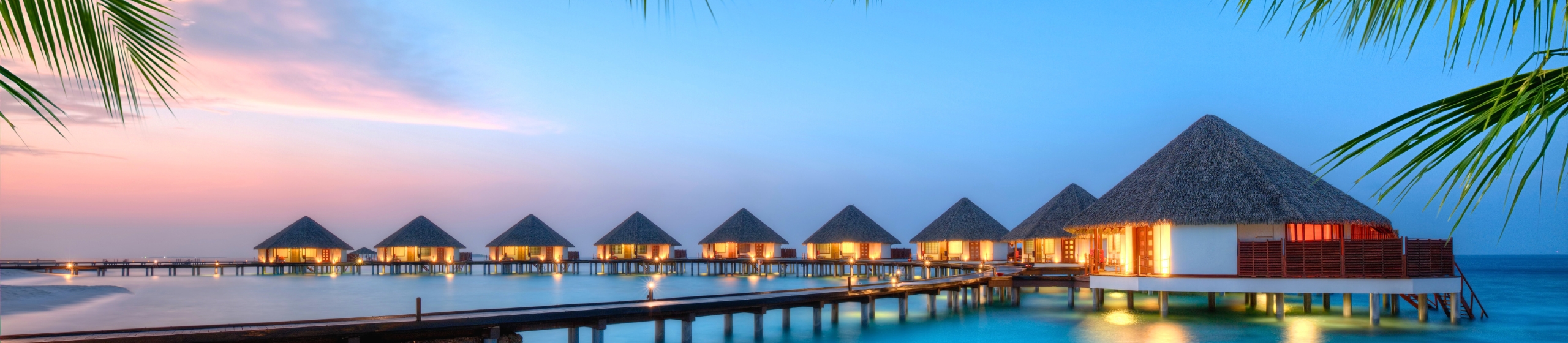 Overwater bungalows at sunset in the Maldives over a calm blue lagoon.